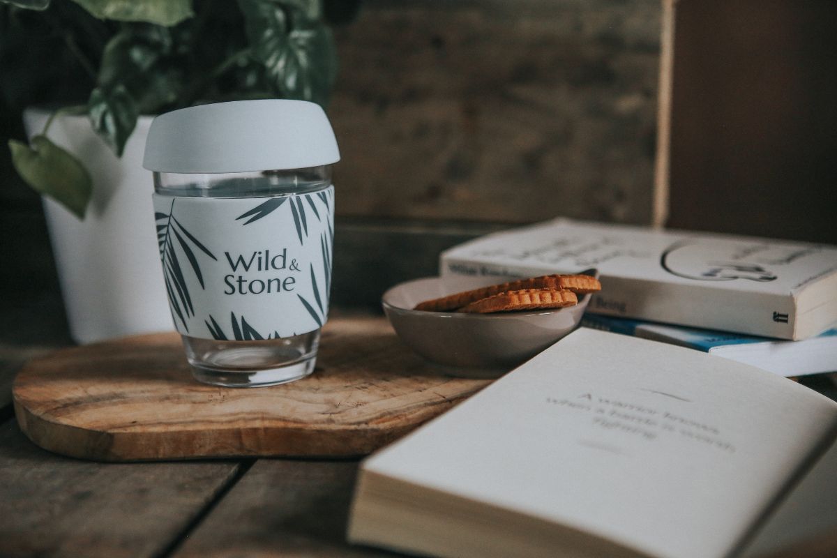 Wild & stone reusable coffee cup next to book.