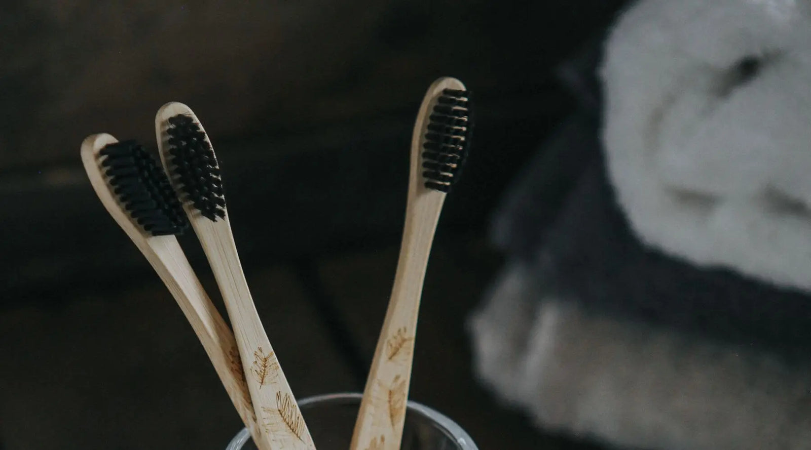Bamboo toothbrushes in glass jar with towels in background