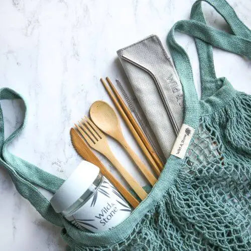 Green tote bag with bamboo cutlery and glass reusable cup inside on a marbled sruface