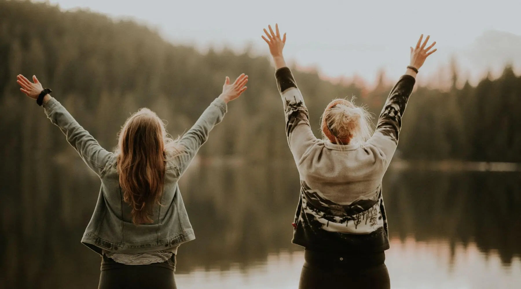 Two women with hand in the air in from of lake