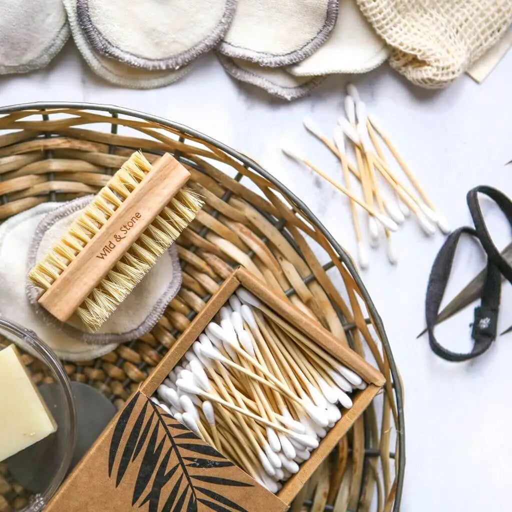 Cotton buds, nail brush, soap, hair ties and makeup remover pads on white marbled surface.