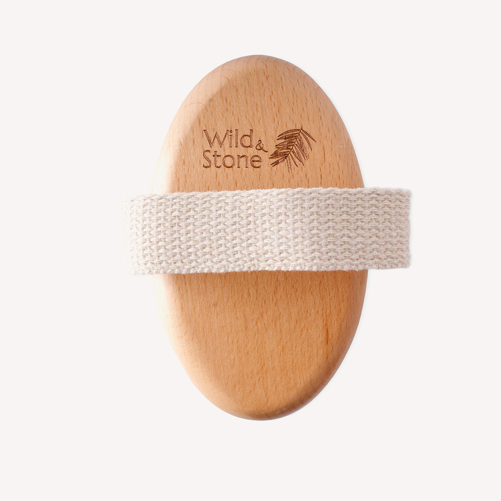 The beechwood top of the natural body brush with a cotton strap and "Wild & Stone" logo.